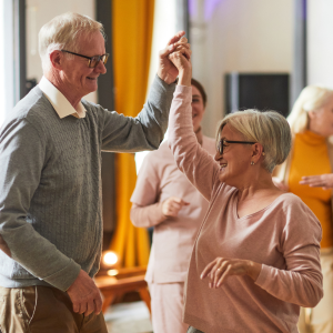 Two elderly people dance with their hand up