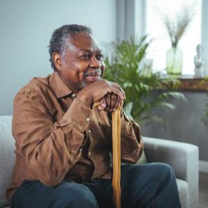 Elderly man thinking with a cane and sitting on a couch