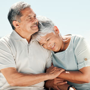 One elderly person leans into another person while smiling and holding hands