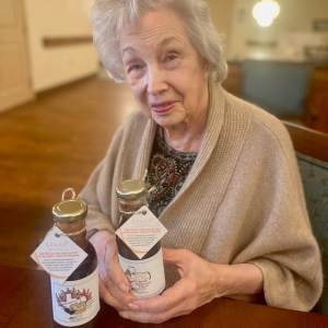 Elderly woman smiling while holding a bottle of barbeque sauce.
