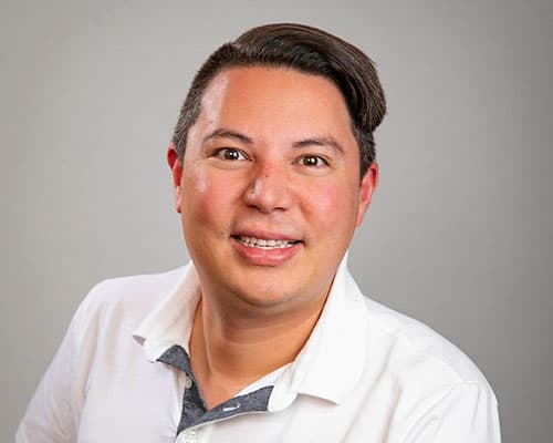 Person smiling in a white collared shirt against a gray background.