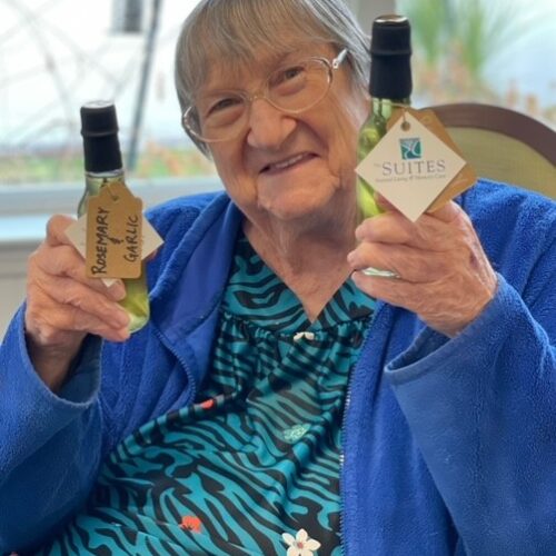 Elderly woman holding two bottles of olive oil, one in each hand.