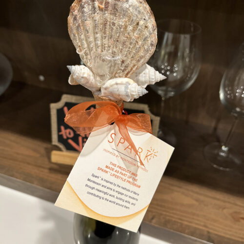 a bottle topped with seashells and a spark tag