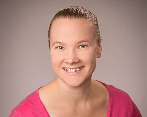 Smiling person with braces, wearing a pink top, against a neutral background.