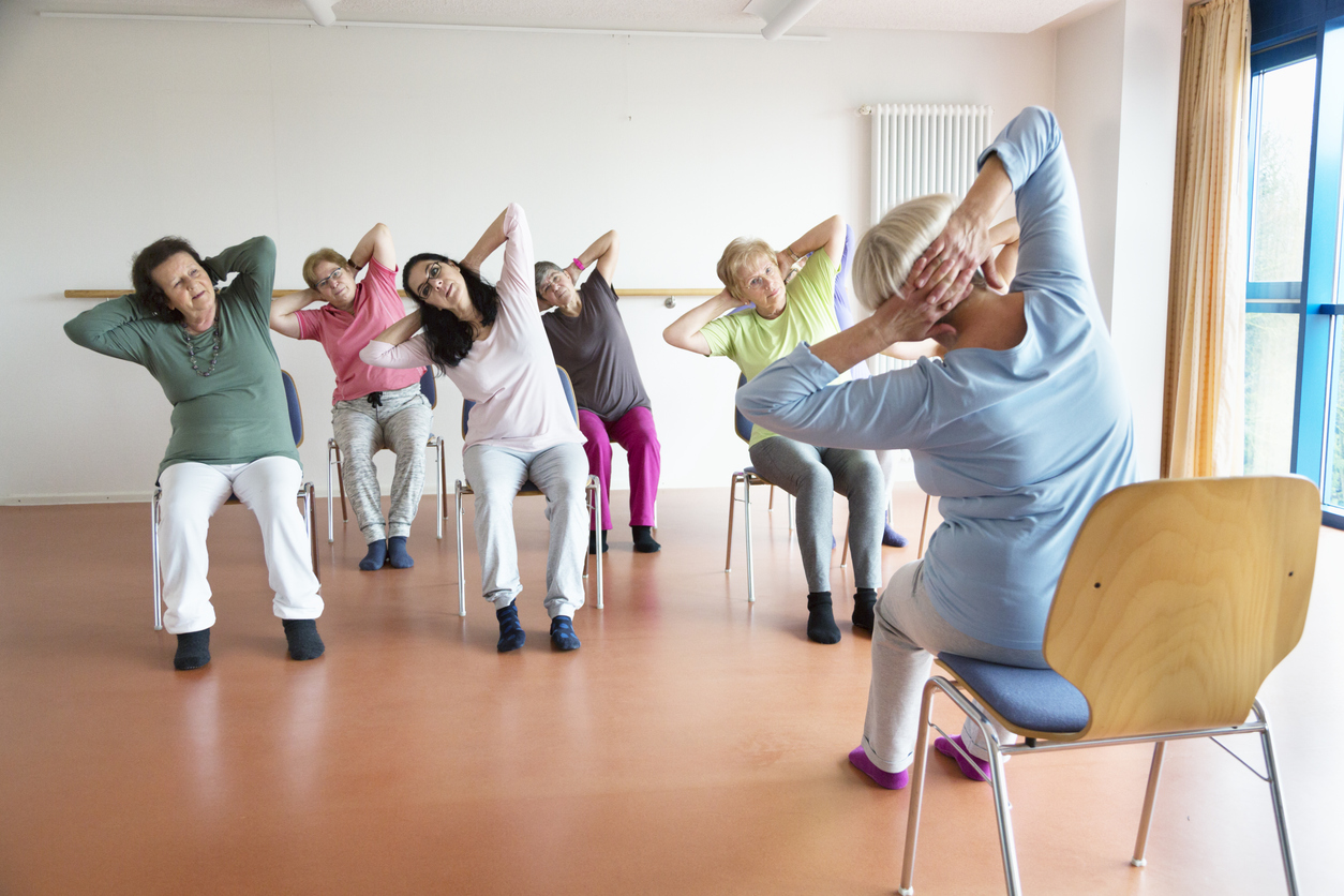 senior women exercising yoga and pilates sitting on chairs, following the instruction of their teacer
