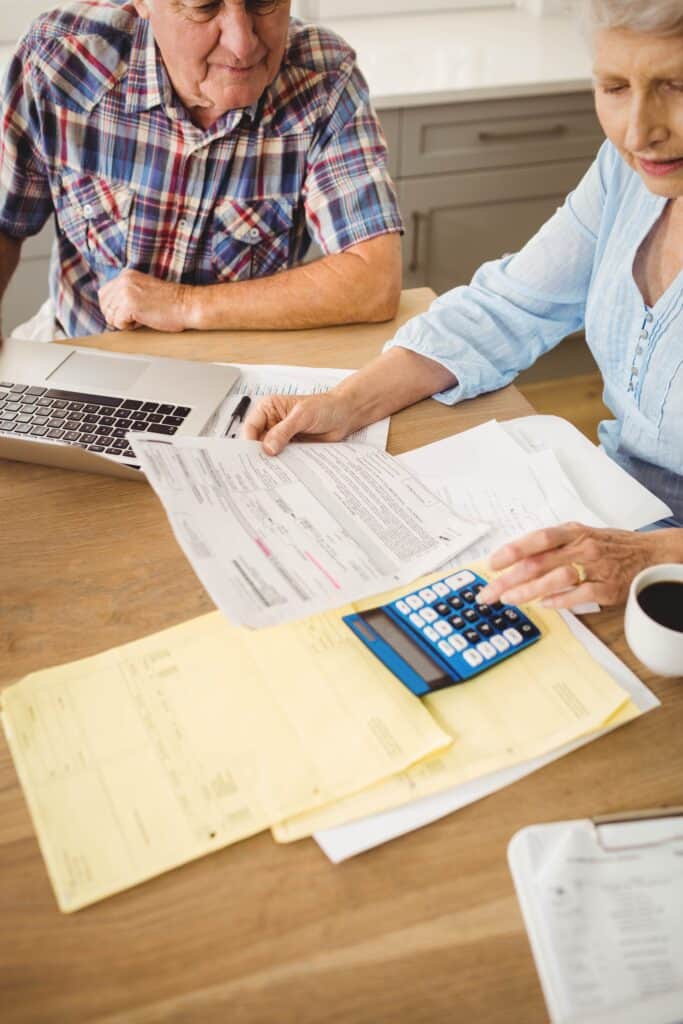 Two elderly individuals at a table reviewing documents with a laptop, calculator, and coffee cup.