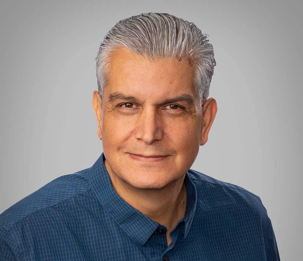 Man with short gray hair and a blue shirt against a gray background.