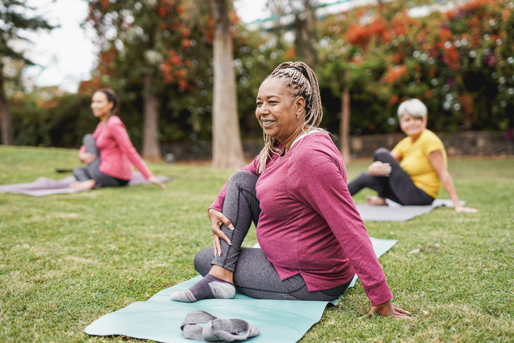 Multiracial women doing yoga exercise with social distance for coronavirus outbreak at park outdoor - Healthy lifestyle and sport concept.
