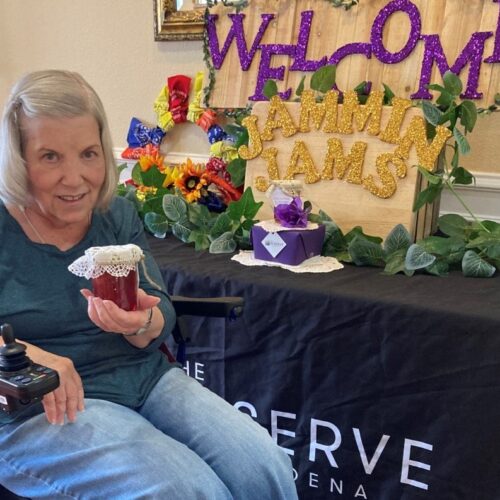 Sweet treat time! An elderly woman in a wheelchair holds a cup of jam with a smile.