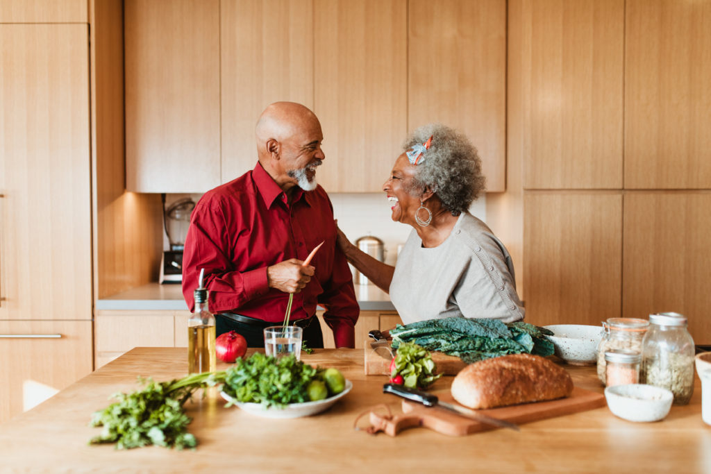 Cheerful senior couple preparing vegan meal in kitchen