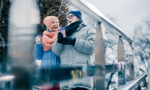 Cheerful elderly people walking with hot chocolate in paper cups and smiling while enjoying winter day outdoors