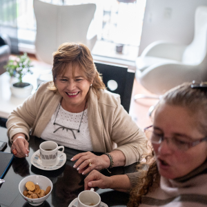 two older women laughing and smiling while drinking coffee