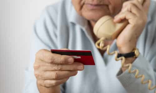 An elderly person holding a red credit card while speaking on a rotary phone.