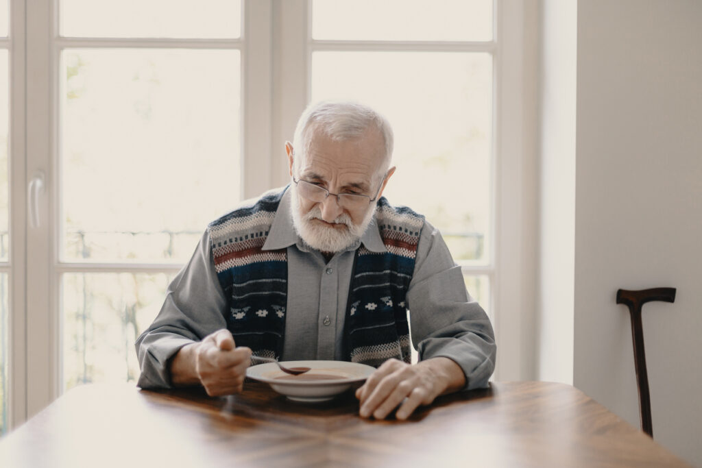 Sad lonely senior man eating soup in empty apartment