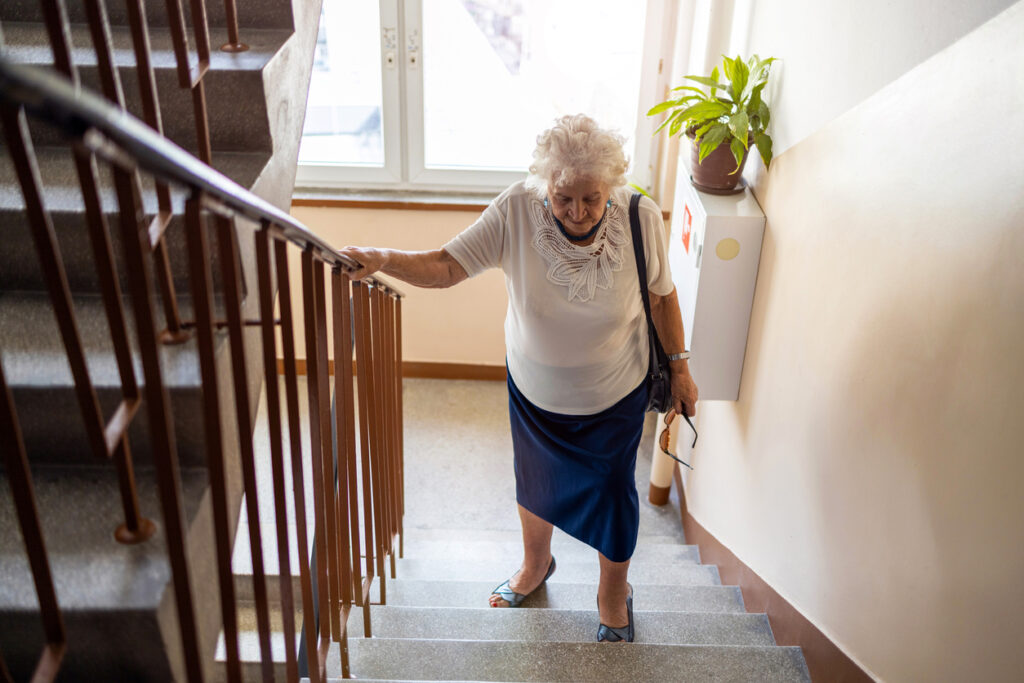 Senior woman climbing staircase with difficulty