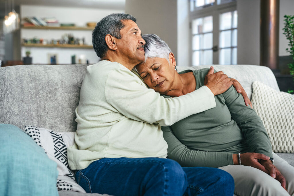 Elderly man holding an elderly woman while sitting on the couch