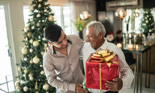 Young man giving christmas present to grandfather on christmas at home