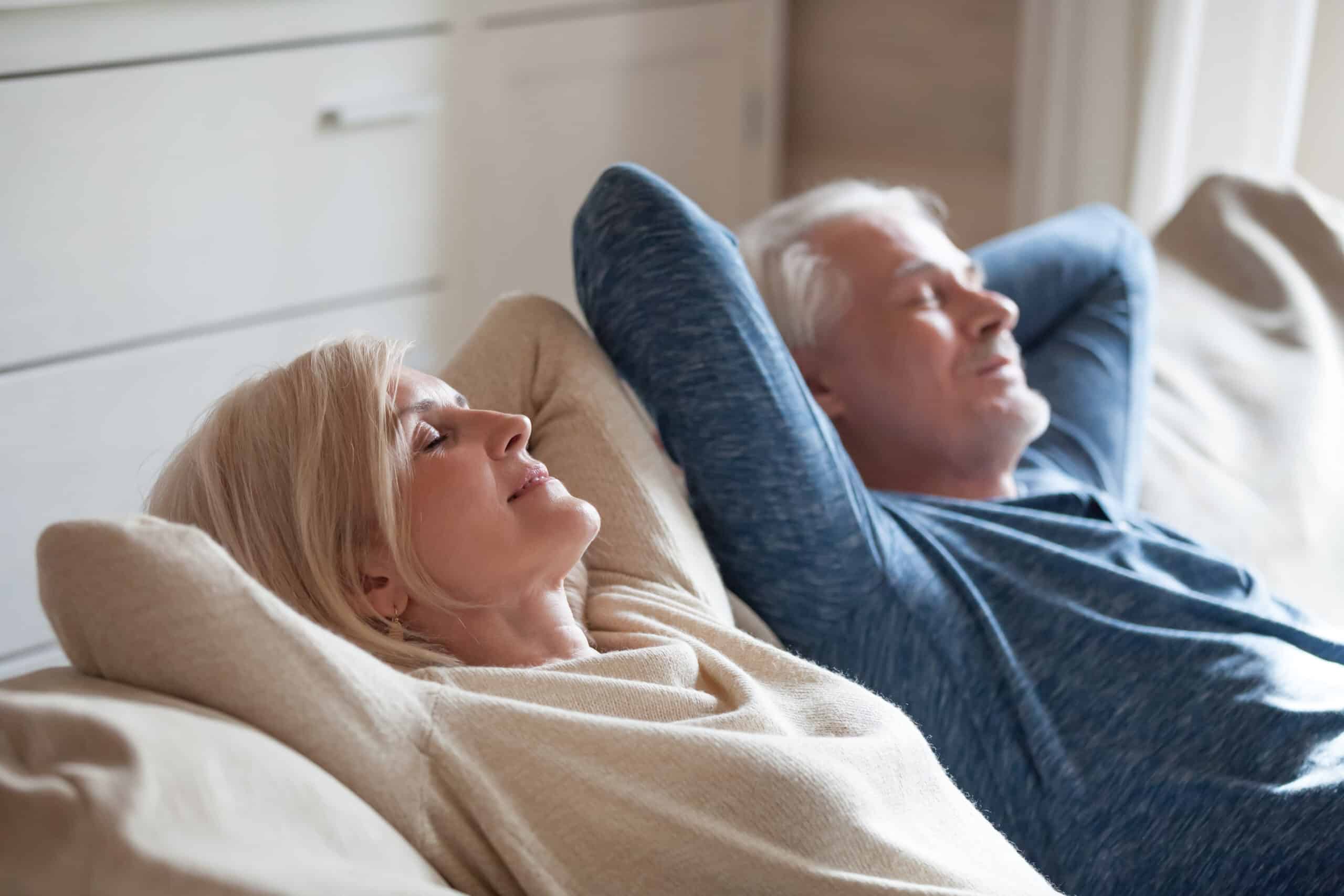 Calm senior mature couple relaxing on soft comfortable sofa having daytime nap together.
