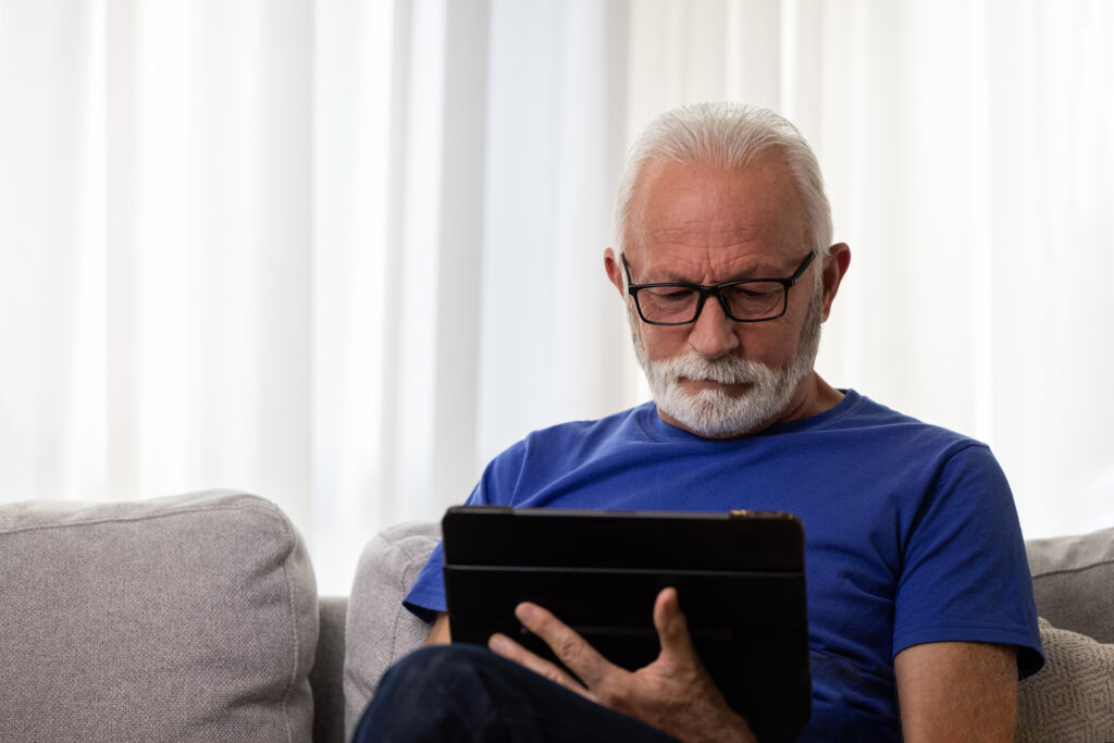 Elderly man reading news on digital tablet. Mature male wearing glasses and using portable computer at home