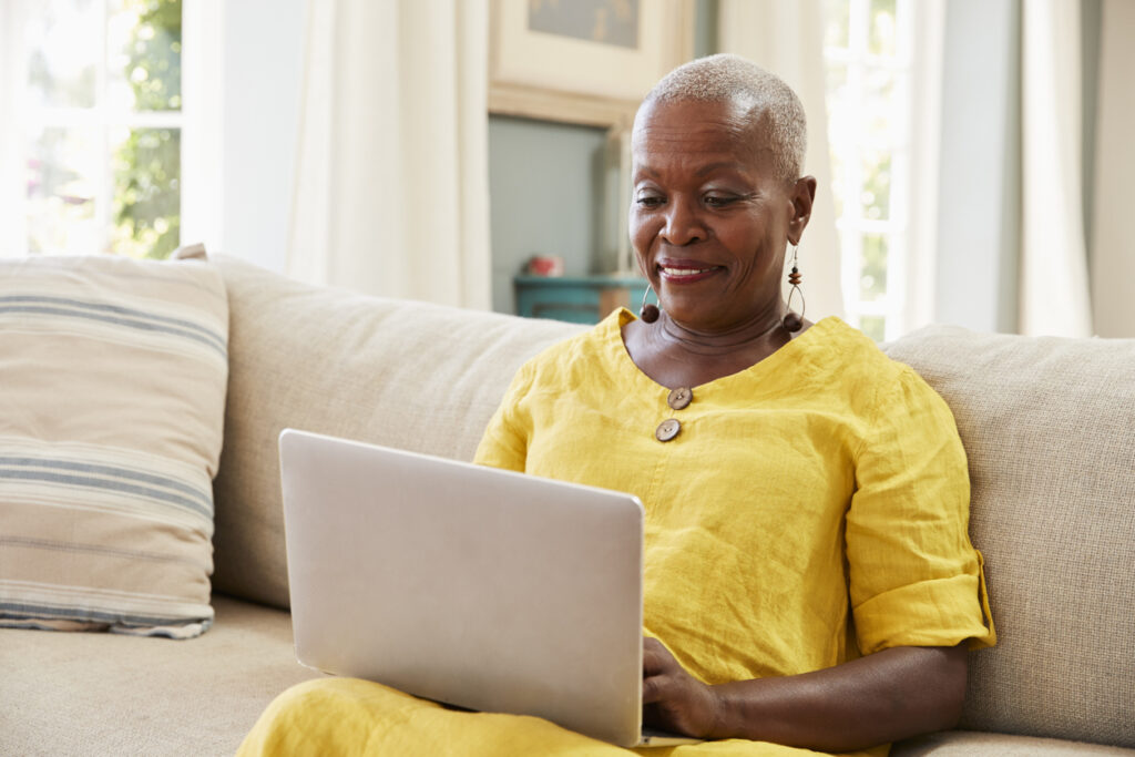 Senior Woman Sitting On Sofa Using Laptop At Home Together