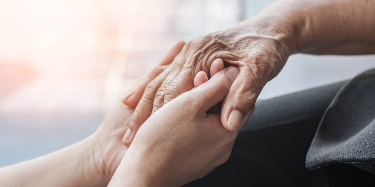 Younger person holding the hands of an elderly person.