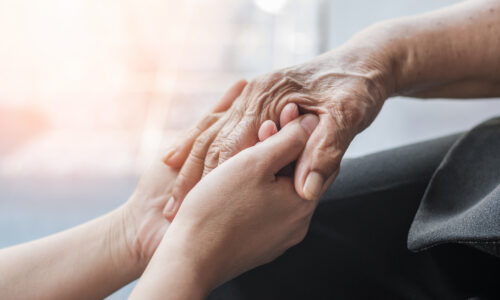 Younger person holding the hands of an elderly person.
