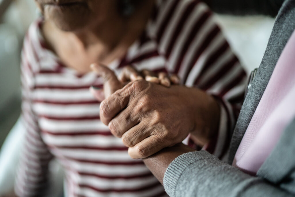 Caregiver and senior woman holding hands at home