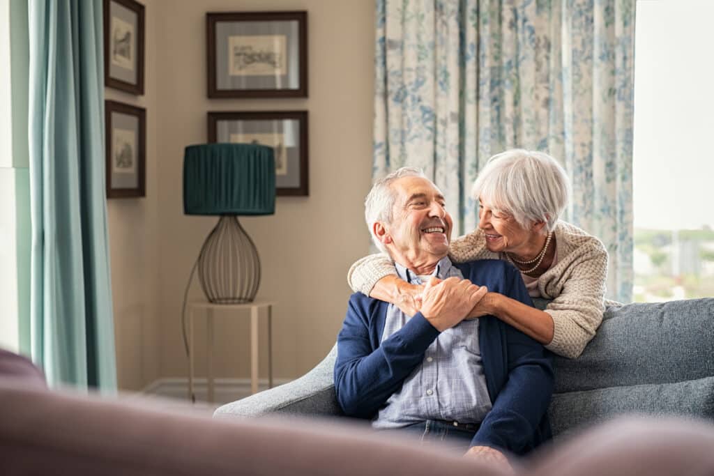 Happy senior woman embracing her husband at home while laughing together