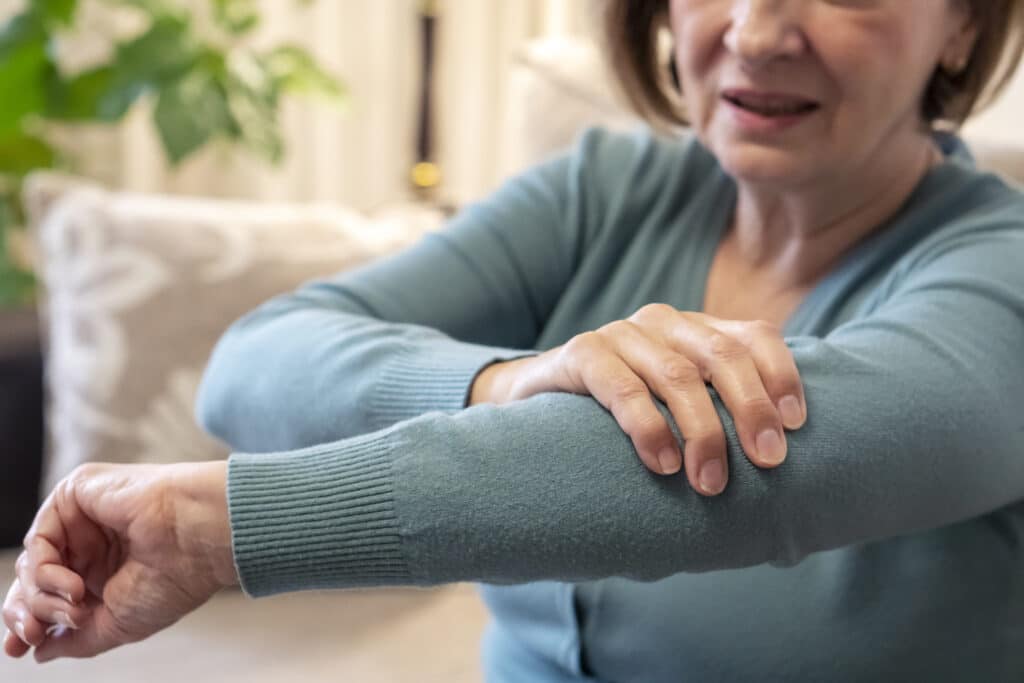 Senior woman sitting on the sofa and touching her elbow.