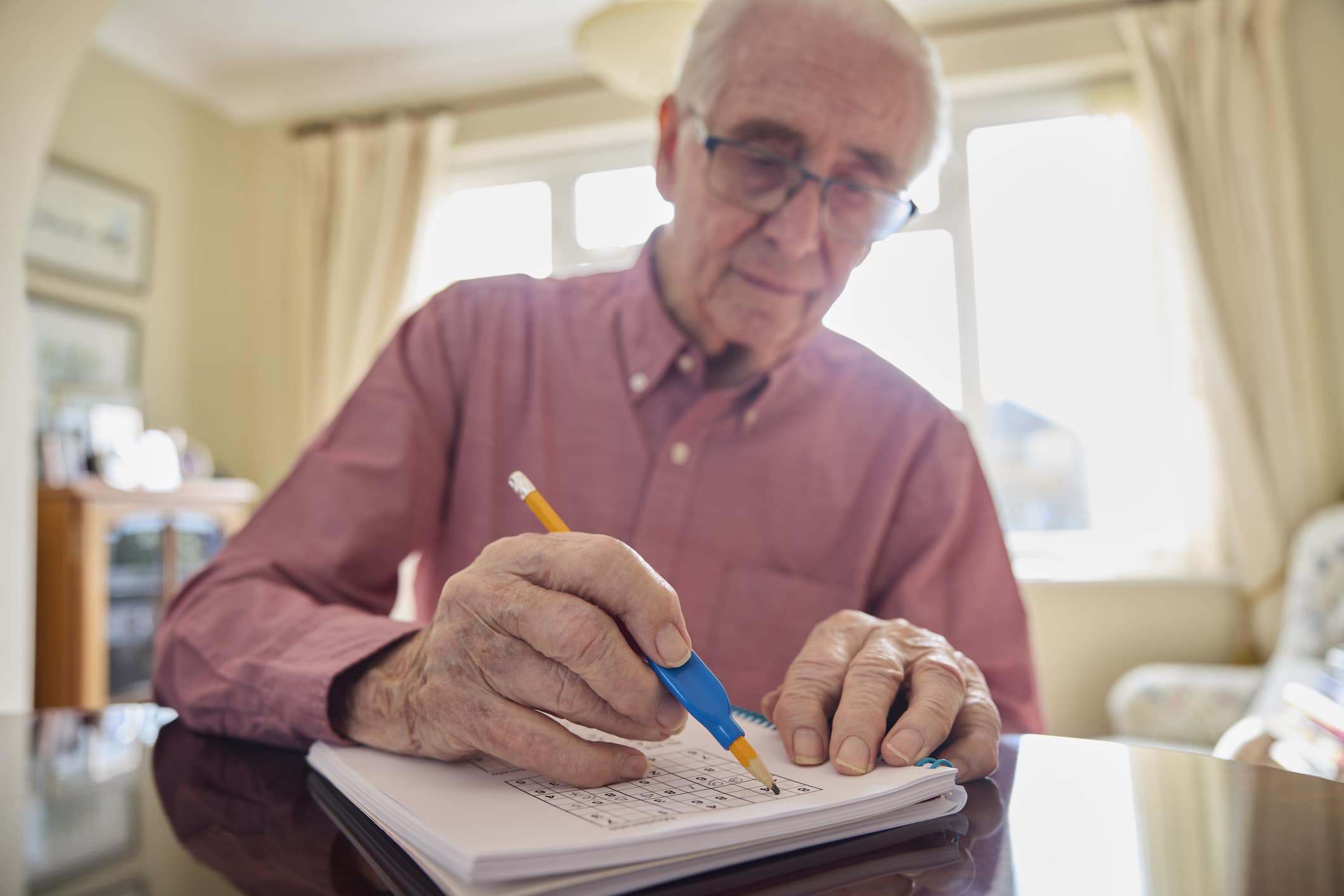 Senior Man With Arthritis Using Grip Aid On Pencil To Write In Sudoku Puzzle Book