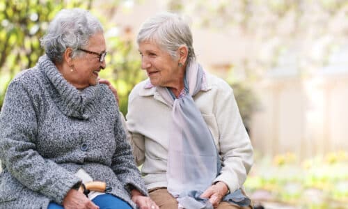 Two elderly women sitting on bench in park smiling happy life long friends enjoying retirement