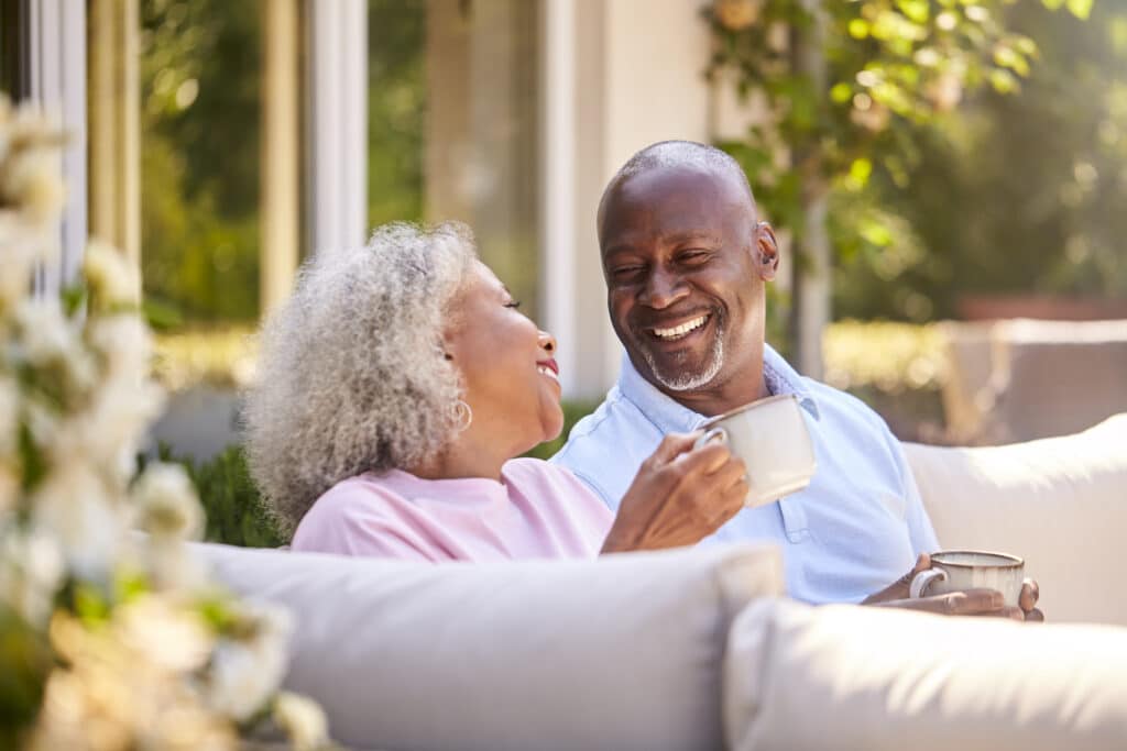 Retired Couple Sitting Outdoors At Home Having Morning Coffee Together