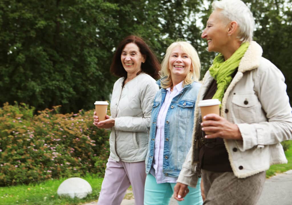 Charming elderly women friends are walking, talking and drinking coffee. Summer day in the park.