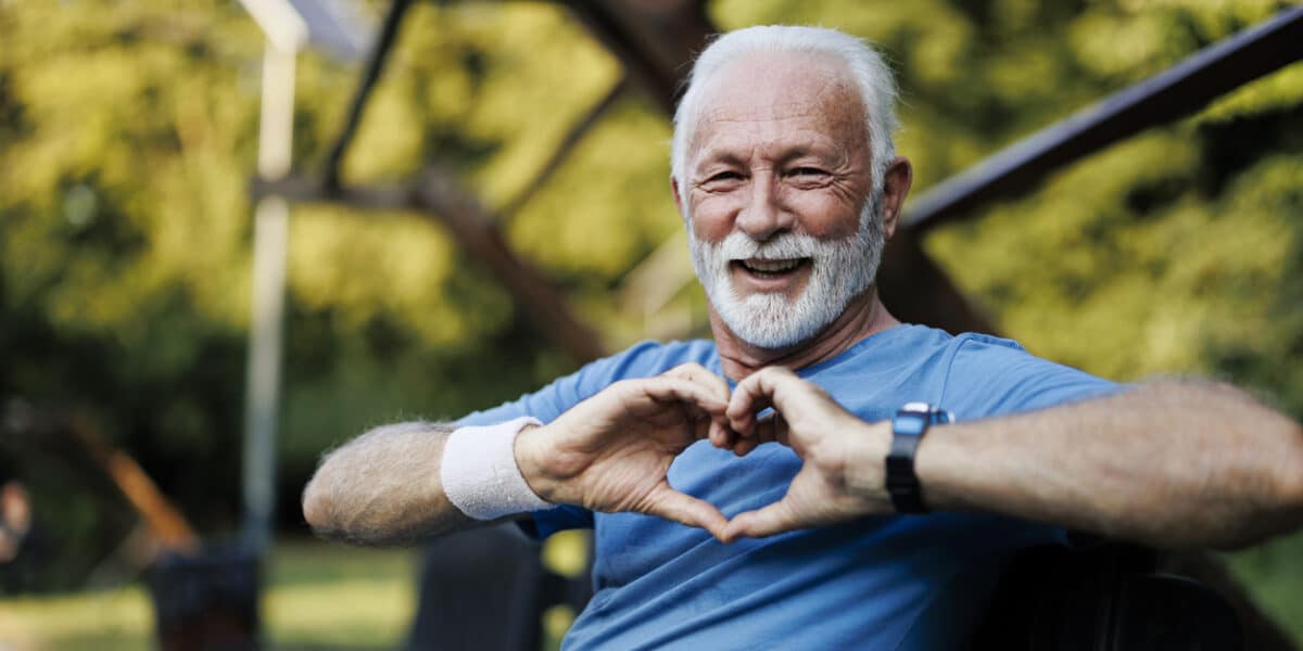 Portrait of a senior sporty man in nature showing a heart-shaped symbol