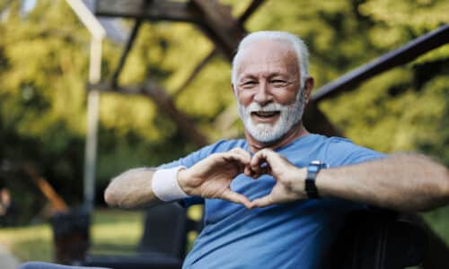 Portrait of a senior sporty man in nature showing a heart-shaped symbol