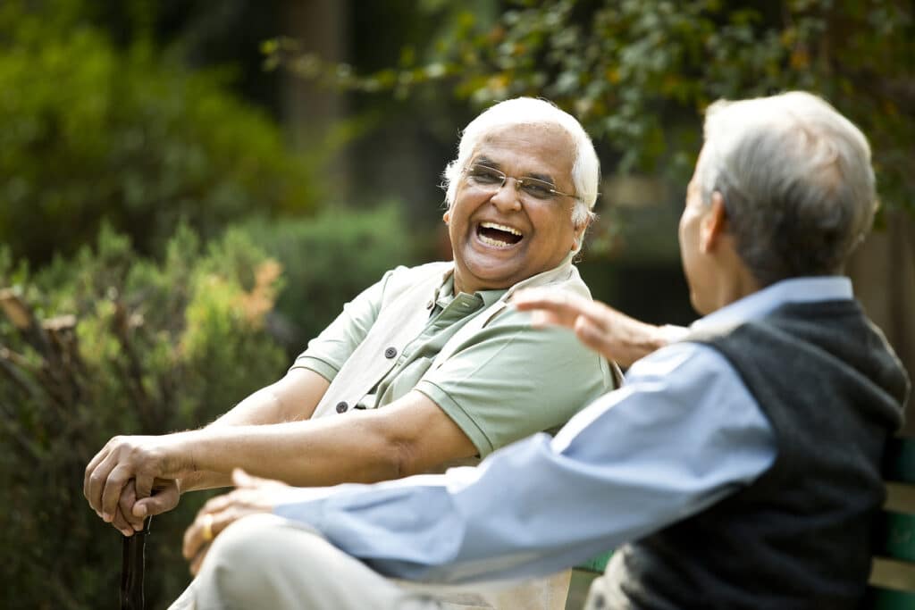 Two retired elderly men sitting on a park bench and having fun

