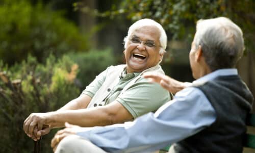 Two retired elderly men sitting on a park bench and having fun