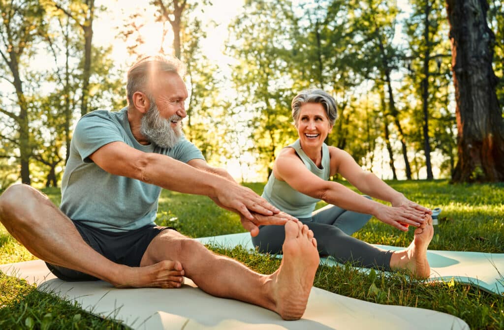 Sporty man and woman with grey hair stretching on yoga mats